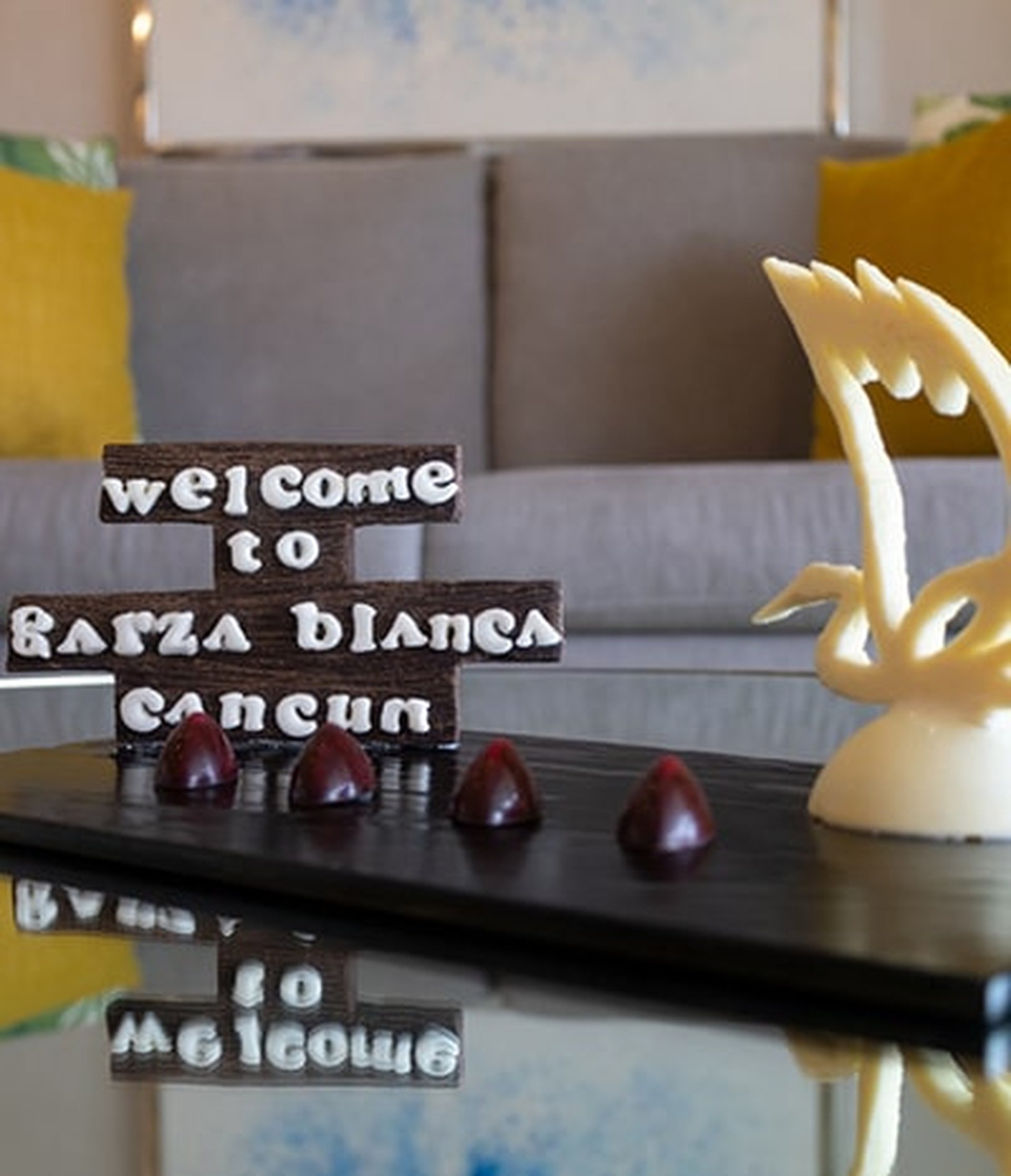 Chocolate sign reading "Welcome to Garza Blanca Cancun" with decorative chocolate swan and truffles on a glass table.