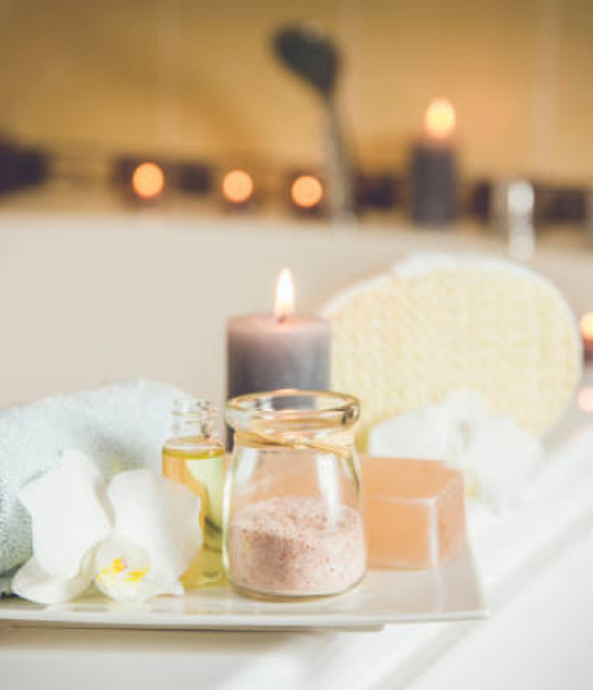 Spa setup with a jar of bath salts, essential oil, orchid, towel, soap, and lit candles, creating a relaxing ambiance.