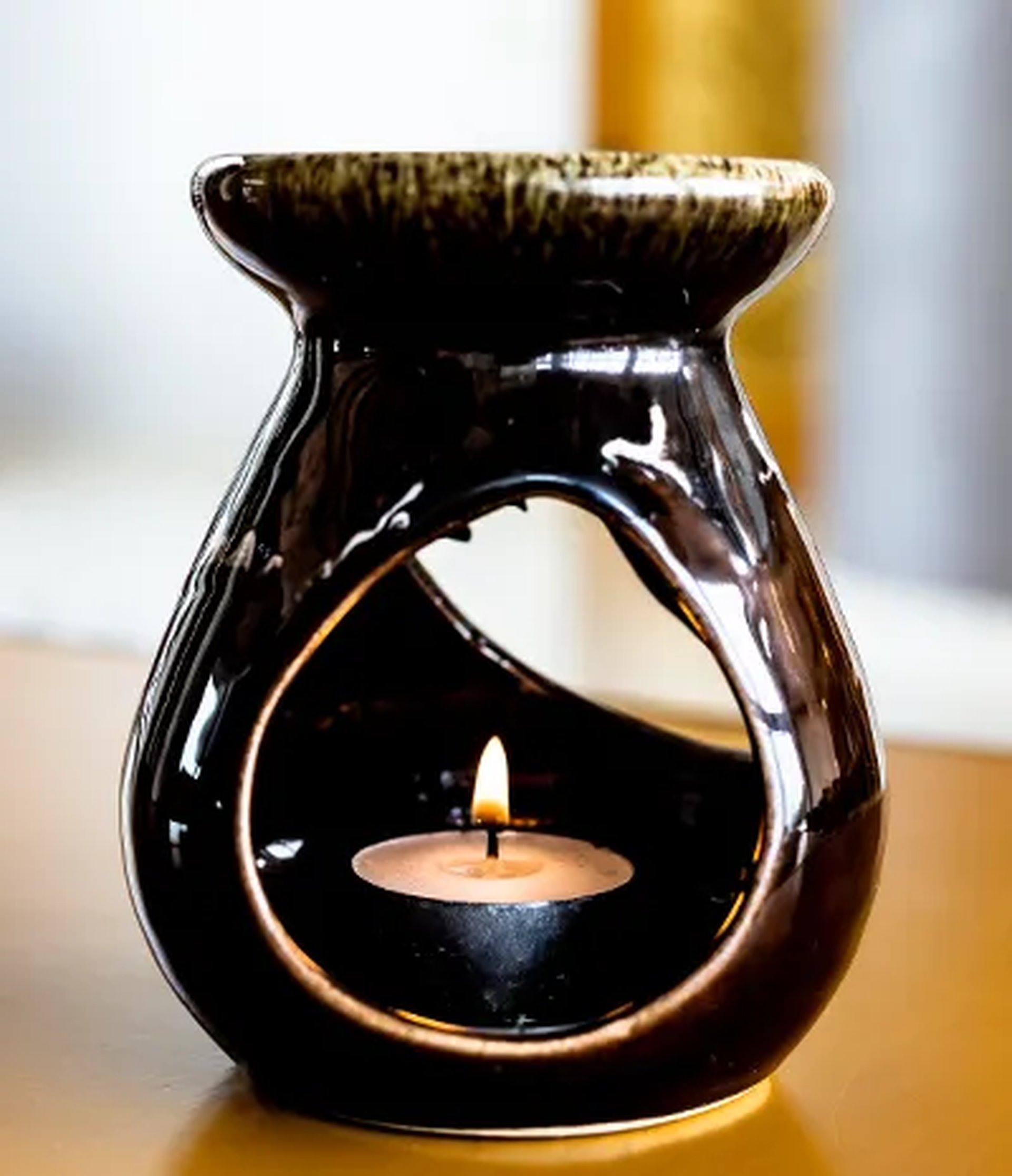 A black ceramic oil burner with a lit tealight candle inside, placed on a reflective surface.