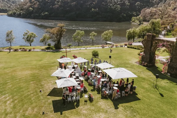 Vista aérea de la ceremonia con sombrillas blancas en el jardín junto al lago