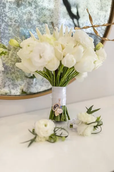 Elegant bouquet of white flowers with a decorative charm, set on a reflective surface with a floral background.