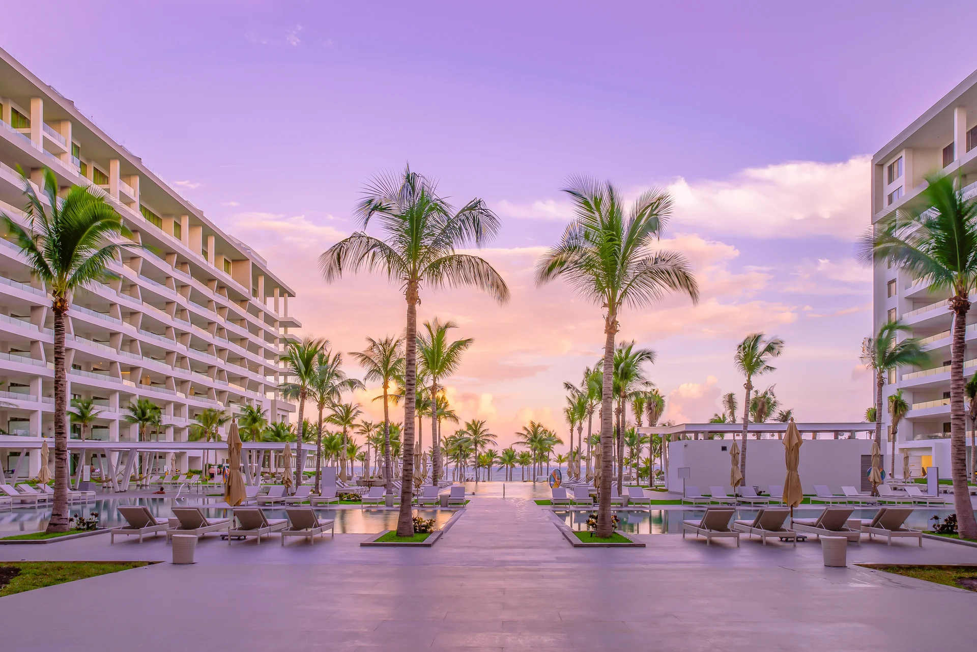 Garza Blanca luxury resort, Mexico: white towers flank a palm-lined pool plaza at sunset; lounge chairs and umbrellas await guests.