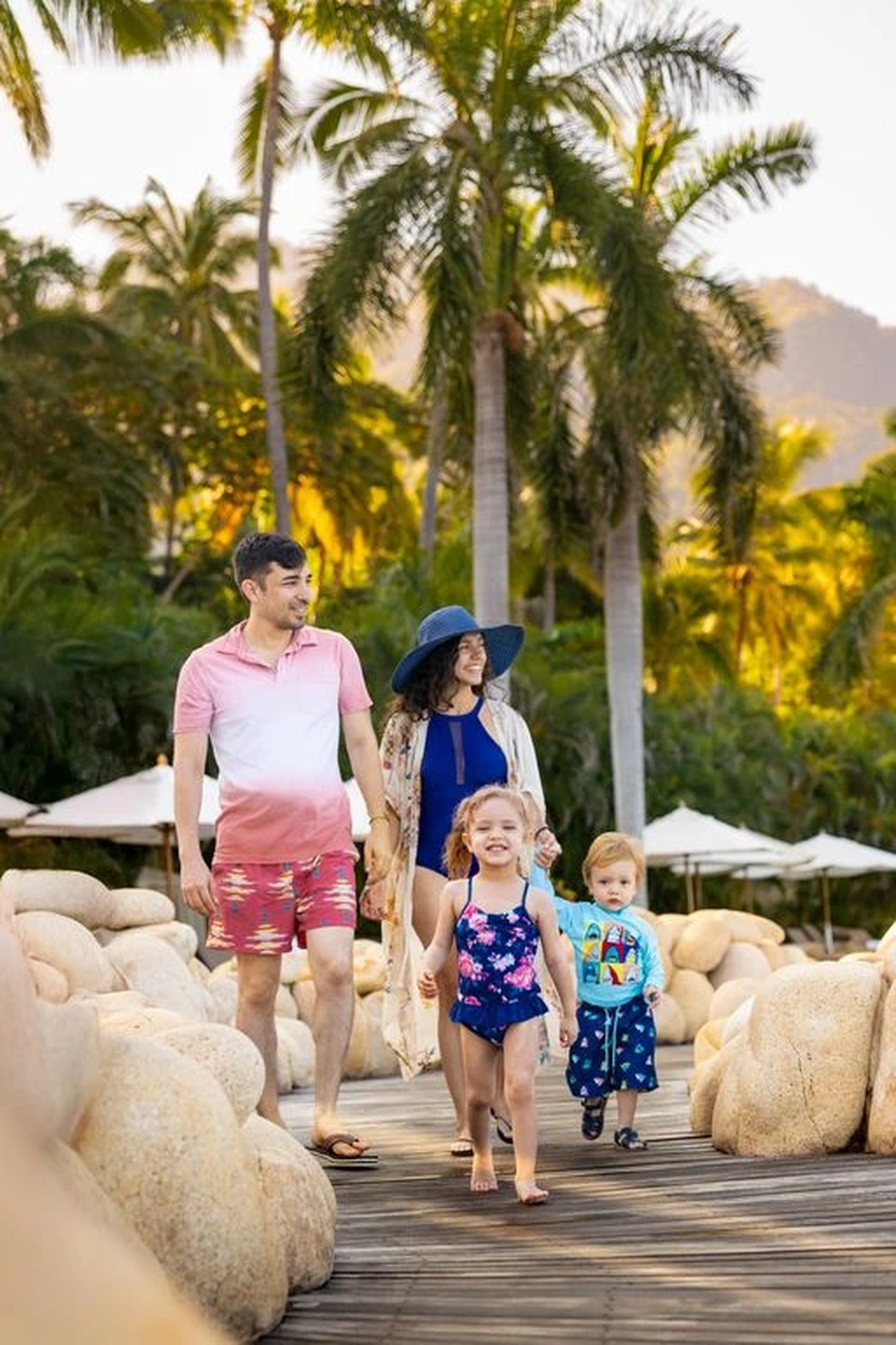 Family of four strolls along a palm-lined boardwalk at Garza Blanca luxury resort, with tropical gardens and beach views.
