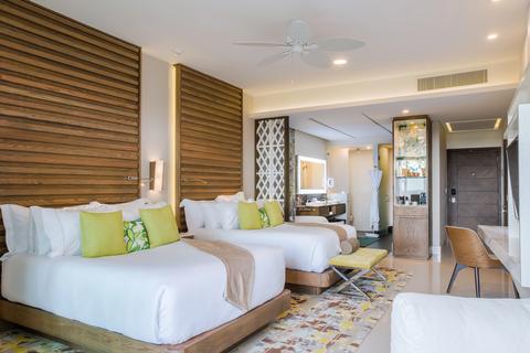 Garza Blanca luxury suite in Mexico: two queen beds, warm wood headboard panels, lime-green accent pillows, and a bright seating area.