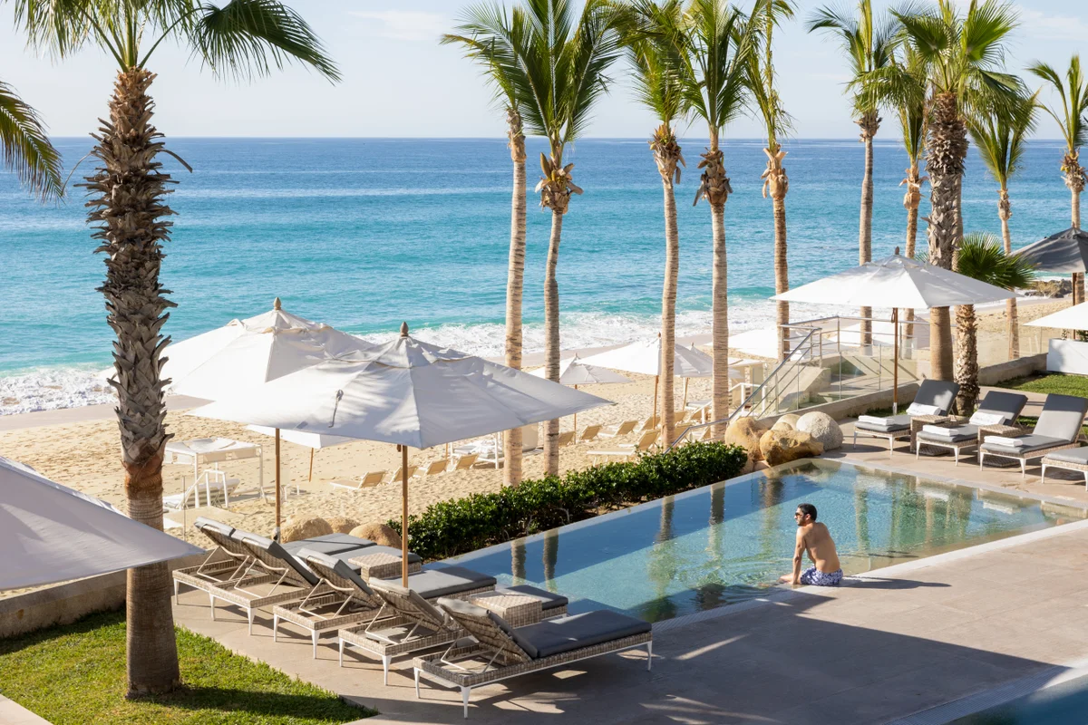 Pool with loungers and palm trees steps from the beach at Garza Blanca Los Cabos
