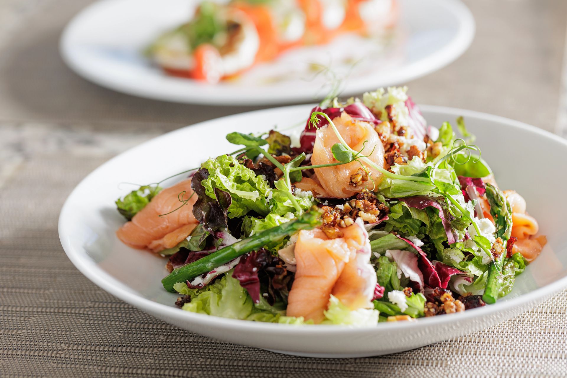 Gourmet salmon salad with mixed greens, walnuts, crumbled cheese, and asparagus on a white plate.