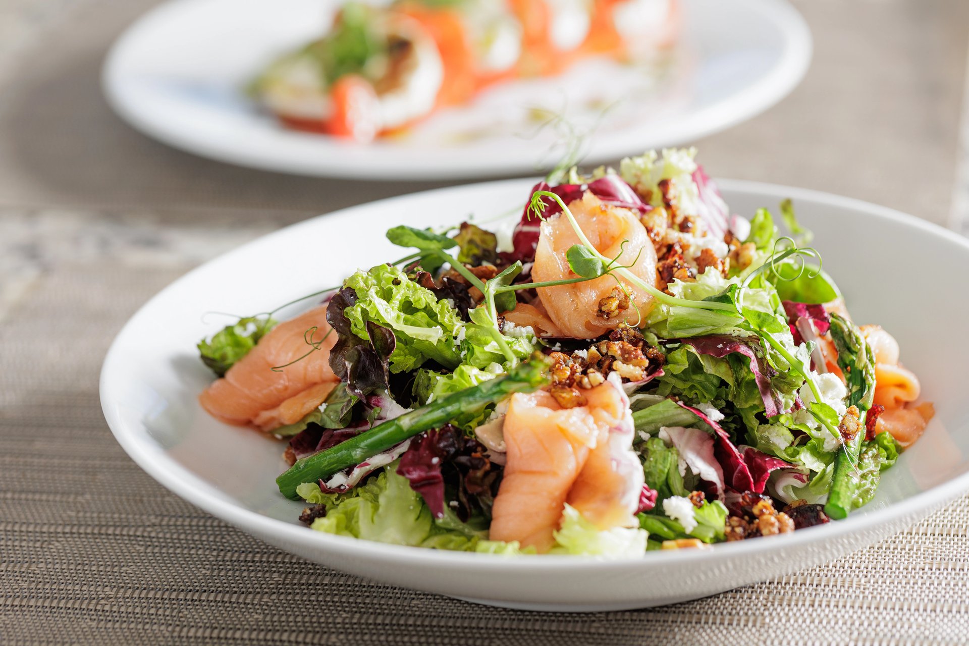Gourmet salmon salad with mixed greens, walnuts, crumbled cheese, and asparagus on a white plate.