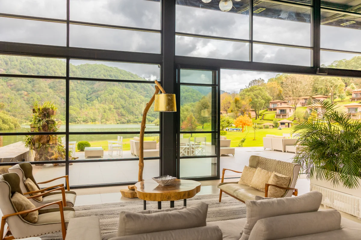 Lounge con sofás y ventanales de piso a techo con vista a la laguna y las cabañas