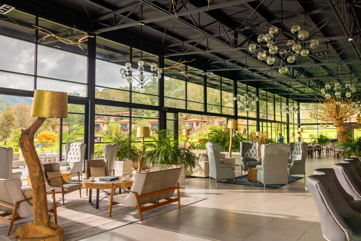 Lounge acristalado y luminoso con sillones y lámparas colgantes con vista a los jardines