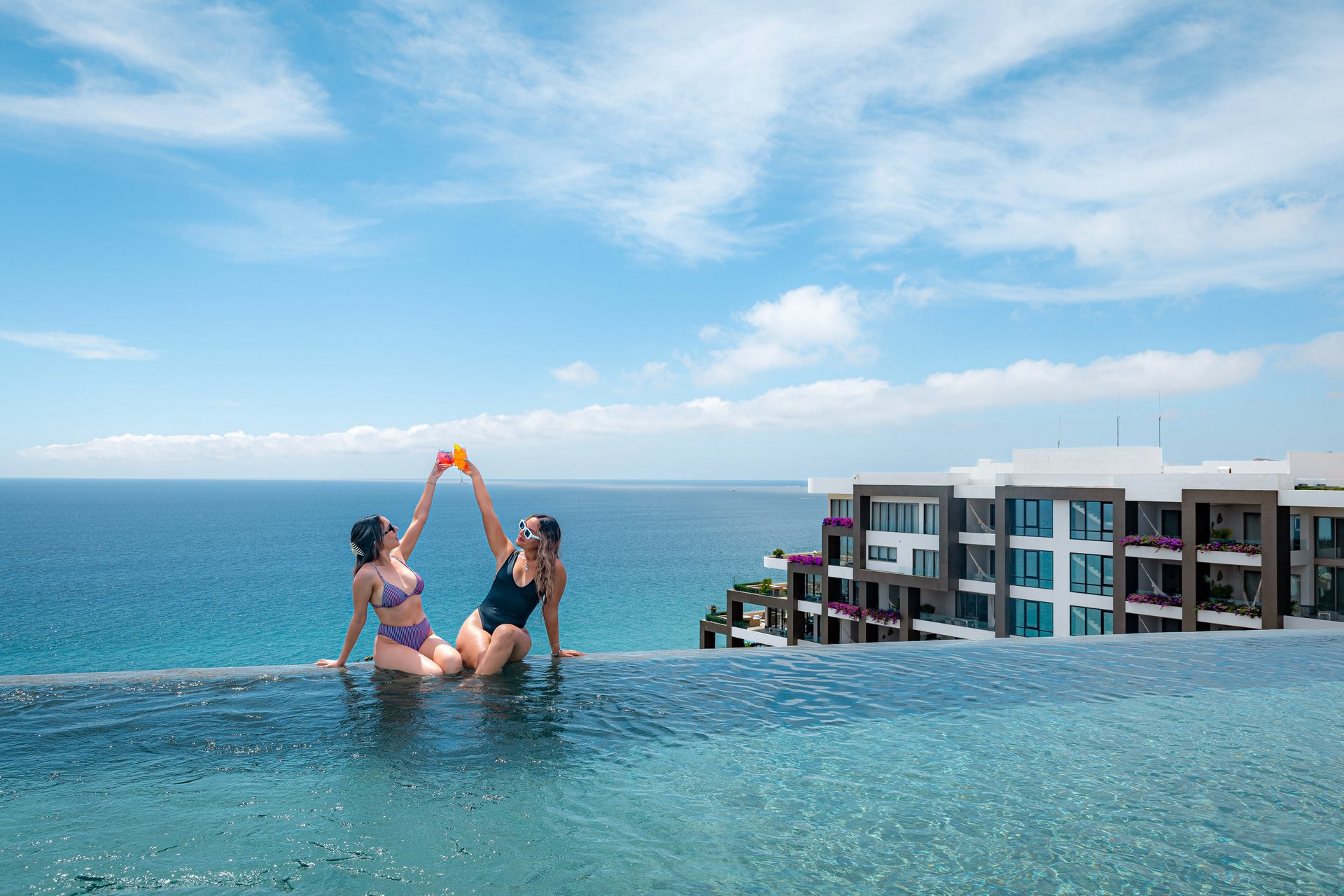 Two guests toast tropical drinks at an infinity pool overlooking the ocean; Garza Blanca luxury resort, Mexico — Escape to the Extraordinary.
