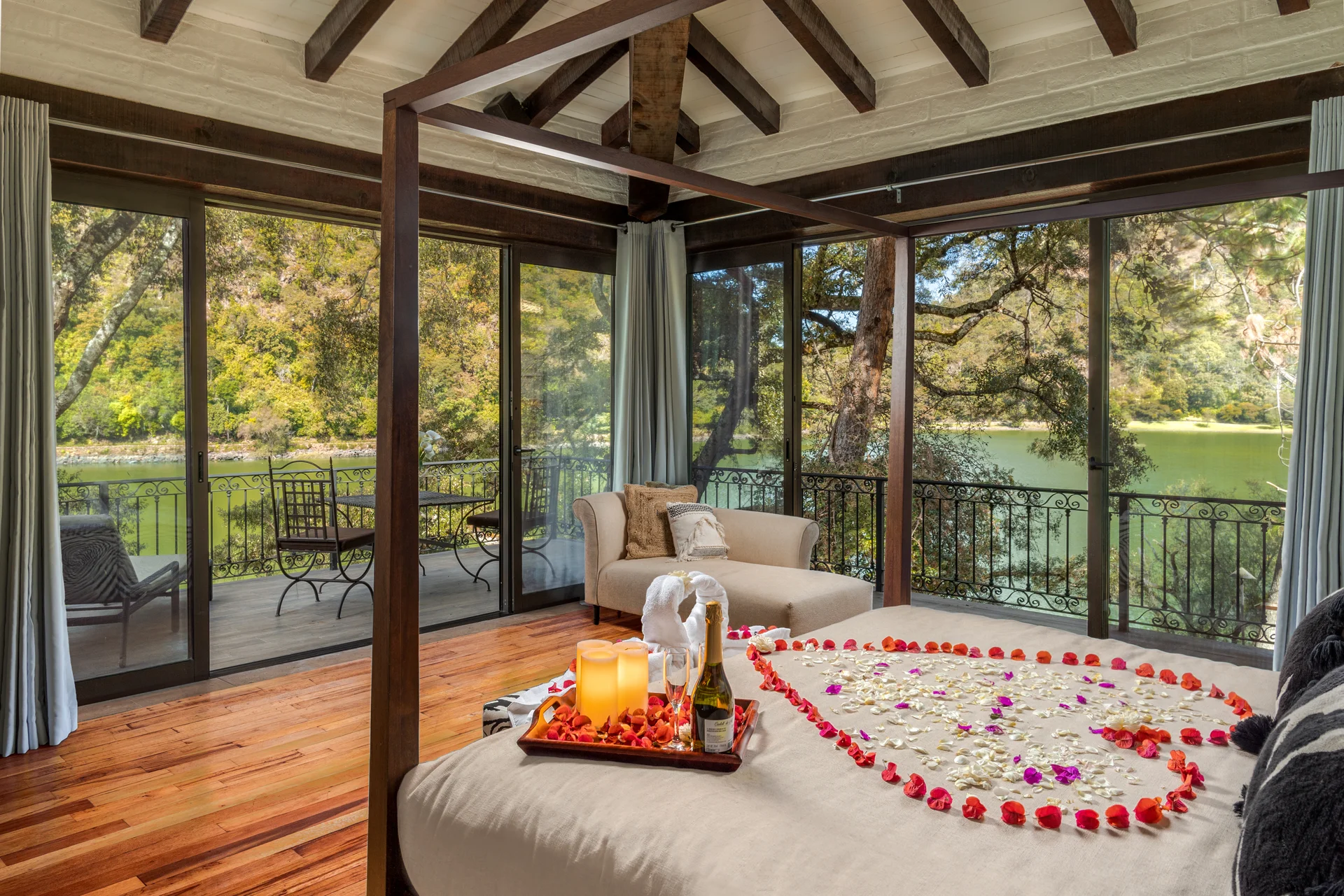 Honeymoon Cabin bed with rose petals arranged in a heart and a private terrace overlooking the forest and lake