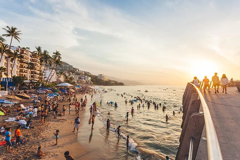 Crowded beach scene in Cancun at sunset, with people enjoying the ocean and sunbathers relaxing.