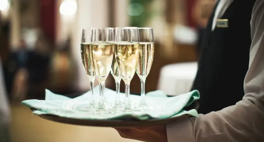 A waiter holds a tray with several glasses of champagne, elegantly arranged in a luxurious setting.