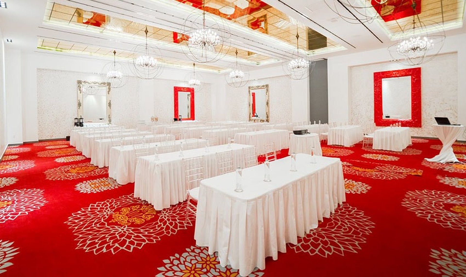 Elegant conference room with vibrant red carpet, white tablecloths, and modern chandeliers, set up for a meeting or event.