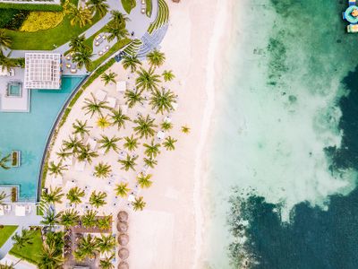 Aerial view of a luxury beachfront resort in Cancun, featuring palm trees, white sand, turquoise water, and elegant poolside areas.