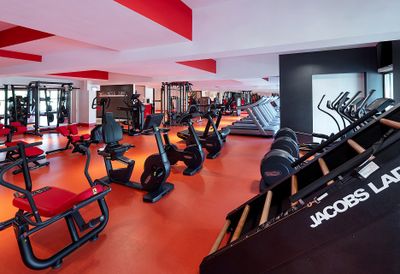 Modern gym with red and black equipment, including exercise bikes, treadmills, and weight machines on an orange floor.