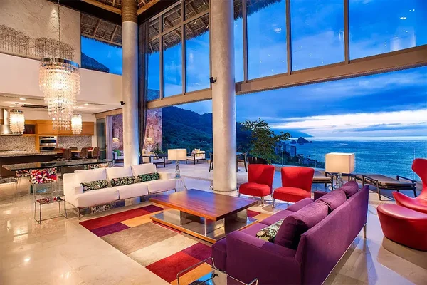 Luxurious open living room with colorful sofas, large windows showcasing an ocean view, modern chandelier, and elegant decor.