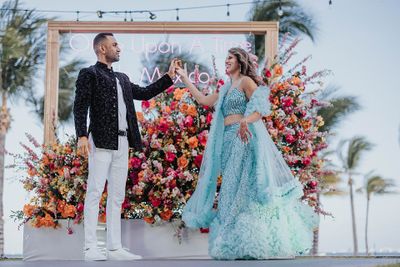A couple in elegant attire dance joyfully in front of a vibrant floral backdrop with "Once Upon a Time in Mexico" sign.