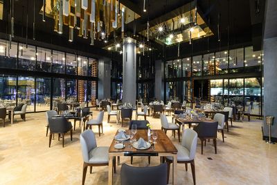 Modern restaurant interior with neatly arranged tables and chairs, elegant lighting, and large glass windows reflecting a stylish ambiance.