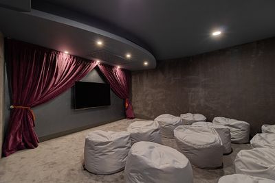 Home theater with a wall-mounted TV, purple curtains, gray walls, and white bean bag chairs on a carpeted floor.