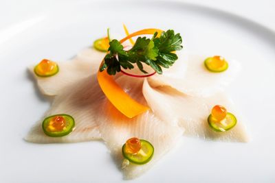 Thinly sliced fish arranged on a plate, garnished with orange roe, jalapeño slices, parsley, and a carrot ribbon.