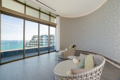 Two round wicker chairs with cushions in a modern room with large windows overlooking the ocean and nearby buildings.