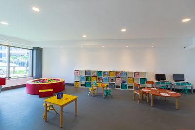 Bright playroom with colorful tables, chairs, and a ball pit. Storage cubbies line the wall. Two computers are on a desk by the wall.