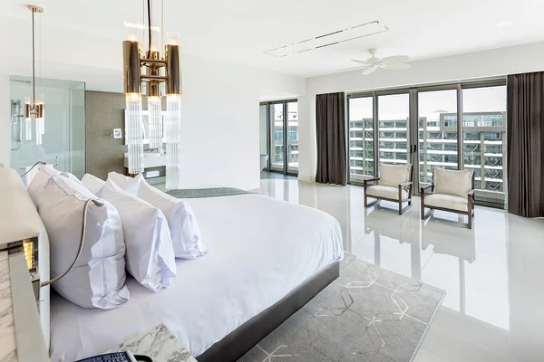 Spacious, modern bedroom with a large bed, glass-walled bathroom, and balcony access. Neutral colors and sleek furniture enhance the airy feel.