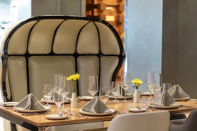 Elegant dining table set with gray napkins, wine glasses, and yellow flowers in a modern restaurant with a unique high-backed chair.