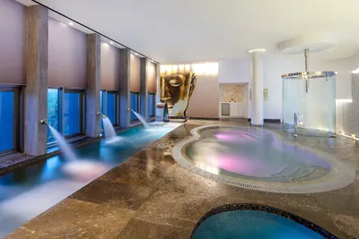Luxurious indoor spa with cascading water features, a large Buddha face mural, and ambient lighting creating a serene atmosphere.