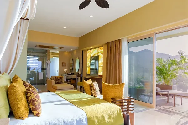 Bright, spacious bedroom with yellow accents, large bed, seating area, and sliding glass doors opening to a balcony with mountain views.