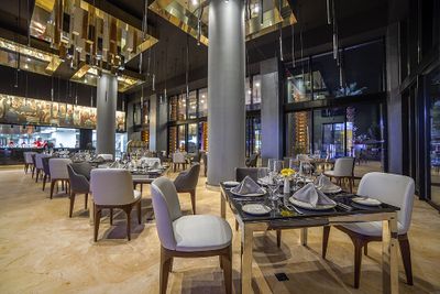 Elegant restaurant interior with modern decor, set tables with white napkins, wine glasses, and soft lighting from overhead fixtures.