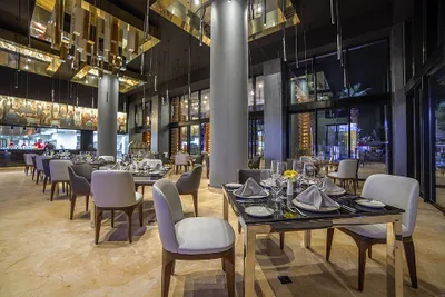 Elegant restaurant interior with modern decor, set tables with white napkins, wine glasses, and soft lighting from overhead fixtures.