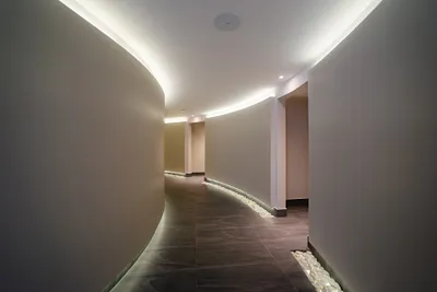 Curved hallway with smooth, beige walls, dim lighting, and a pebble-lined floor, creating a serene and modern ambiance.