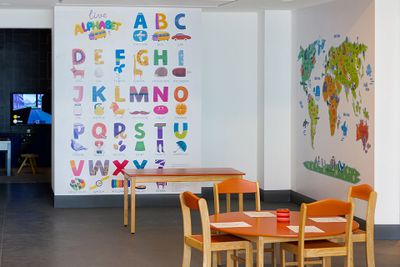 Children's playroom with alphabet wall, colorful table and chairs, and a world map mural.