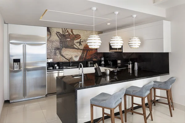Modern kitchen with a sleek island, bar stools, stainless steel appliances, and mosaic backsplash. Pendant lights hang overhead.