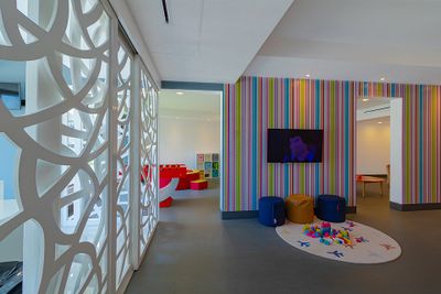Colorful playroom with striped walls, a TV, bean bags on a round rug with toys, and a decorative white partition.