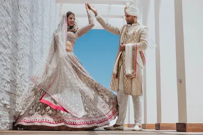 A couple in elegant traditional attire joyfully dances together under a bright blue sky.