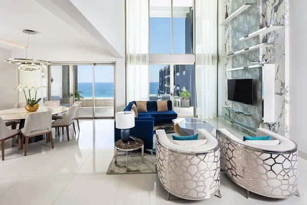 Modern living and dining area with ocean view, featuring elegant furniture, a marble accent wall, and large windows allowing natural light.