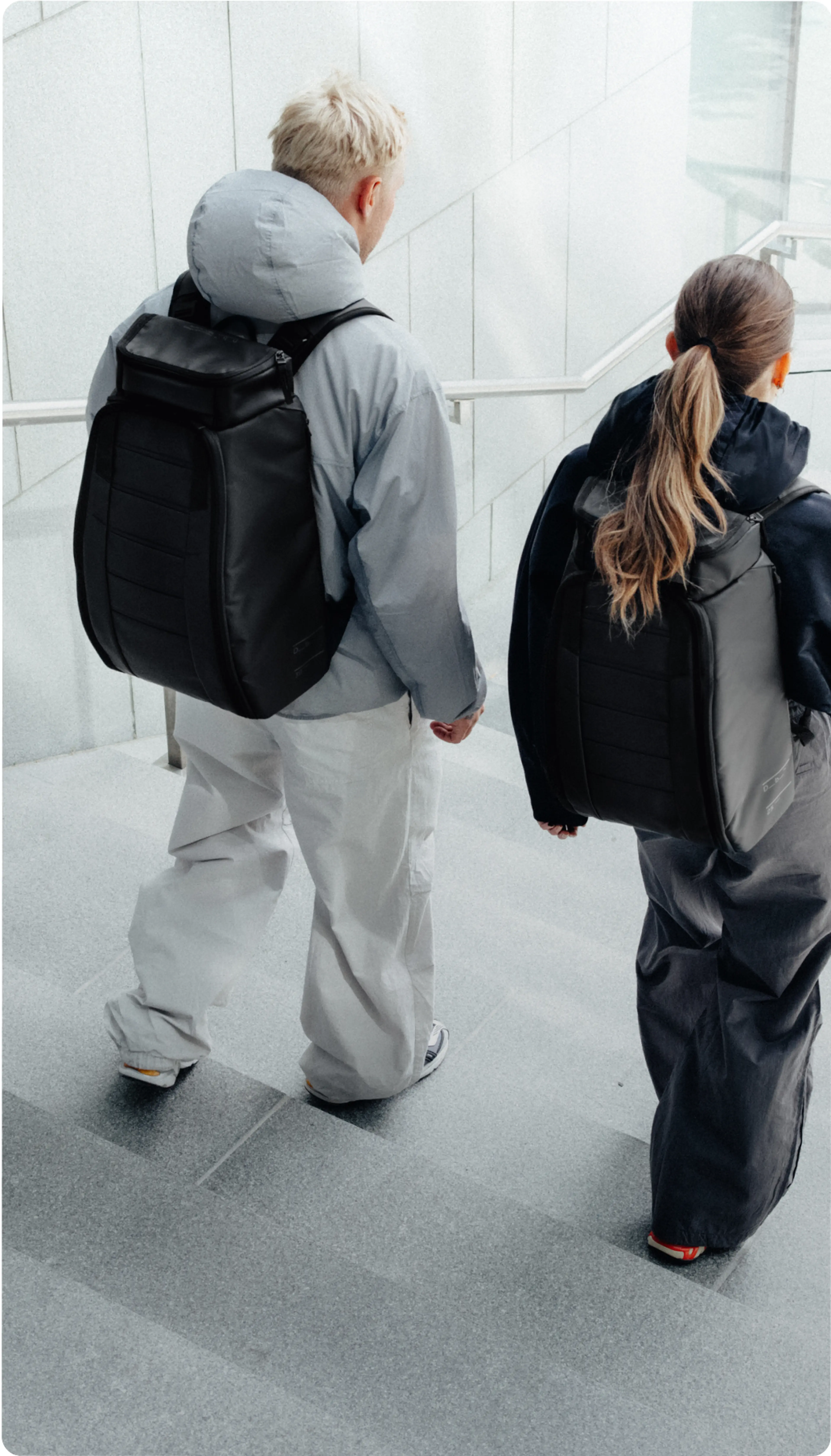 Two people with black backpacks walk down concrete stairs.