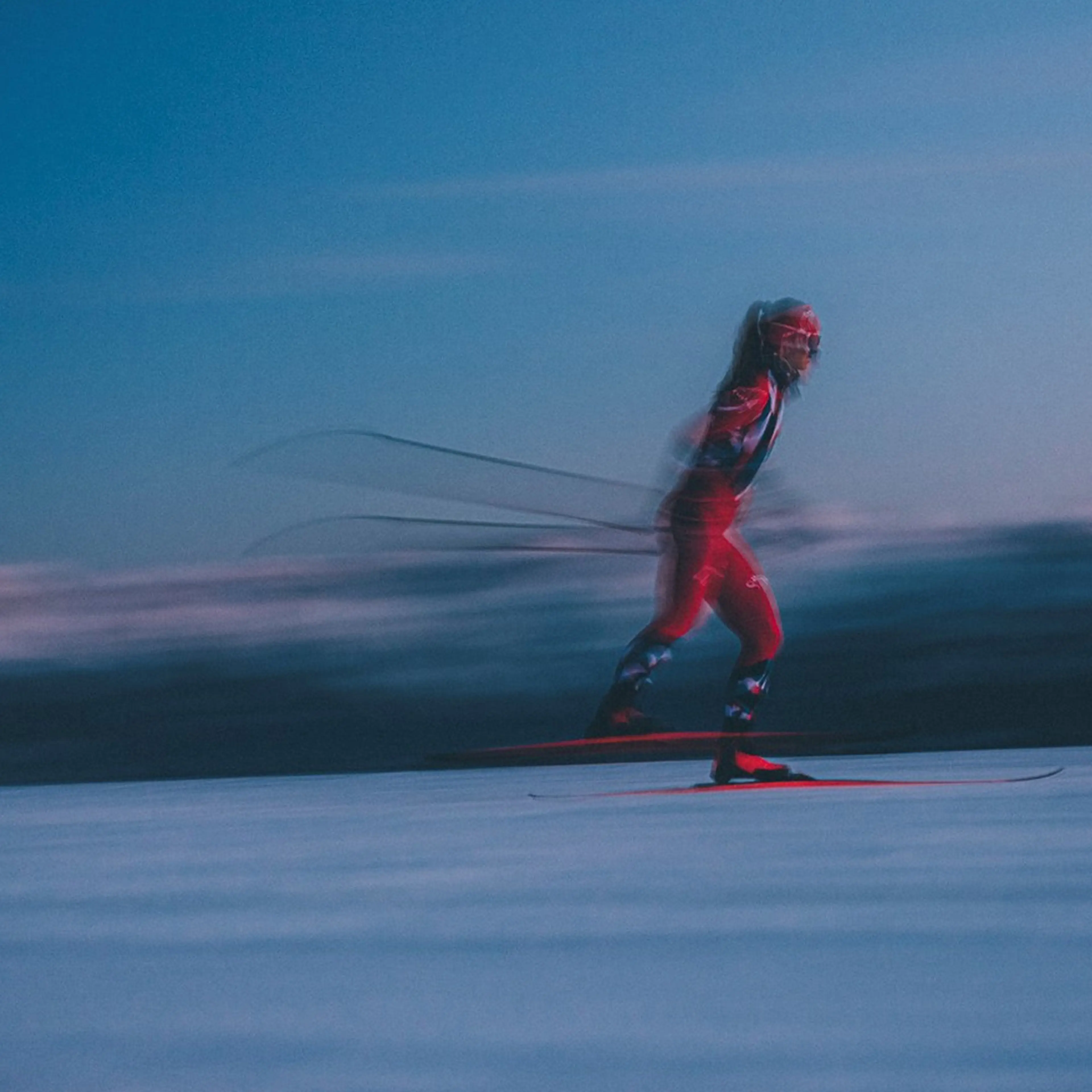 A person in red skiing swiftly on snow under a dusky sky, creating a motion blur effect.