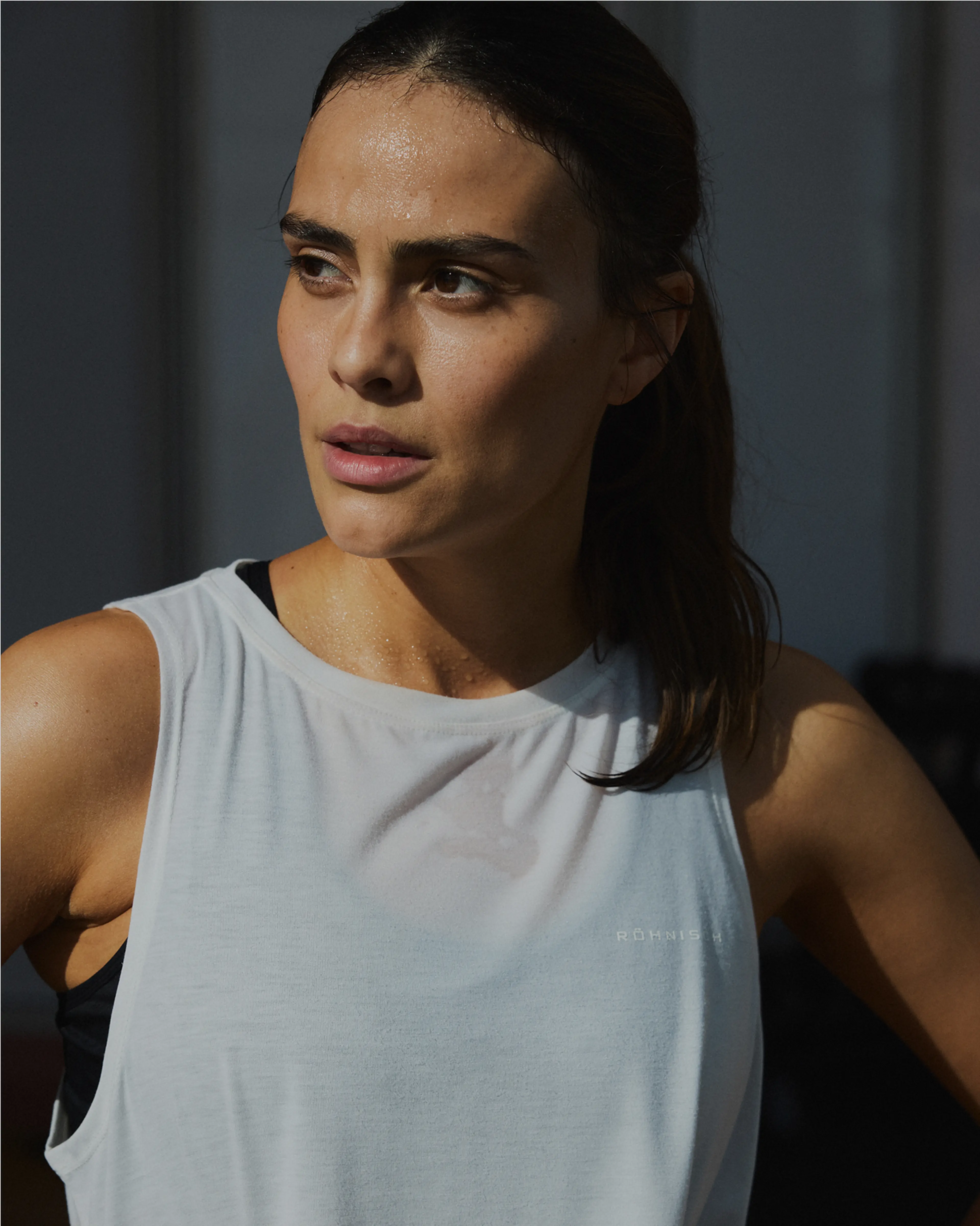 Woman in workout attire, slightly sweaty, looking to the right with a focused expression. She's wearing a light sleeveless top.