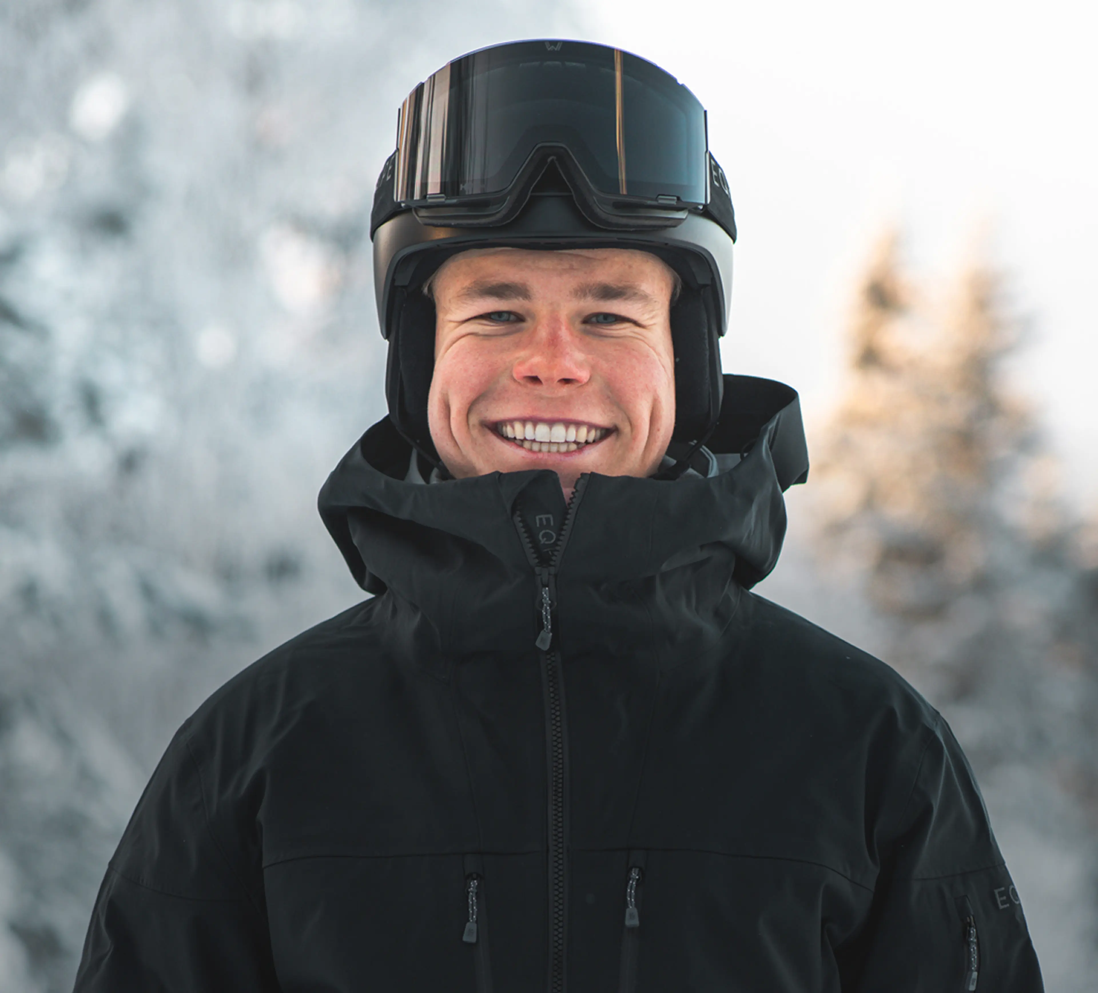 Walter Wallberg wearing a black ski jacket and helmet with goggles, standing outdoors against a snowy, blurred background.
