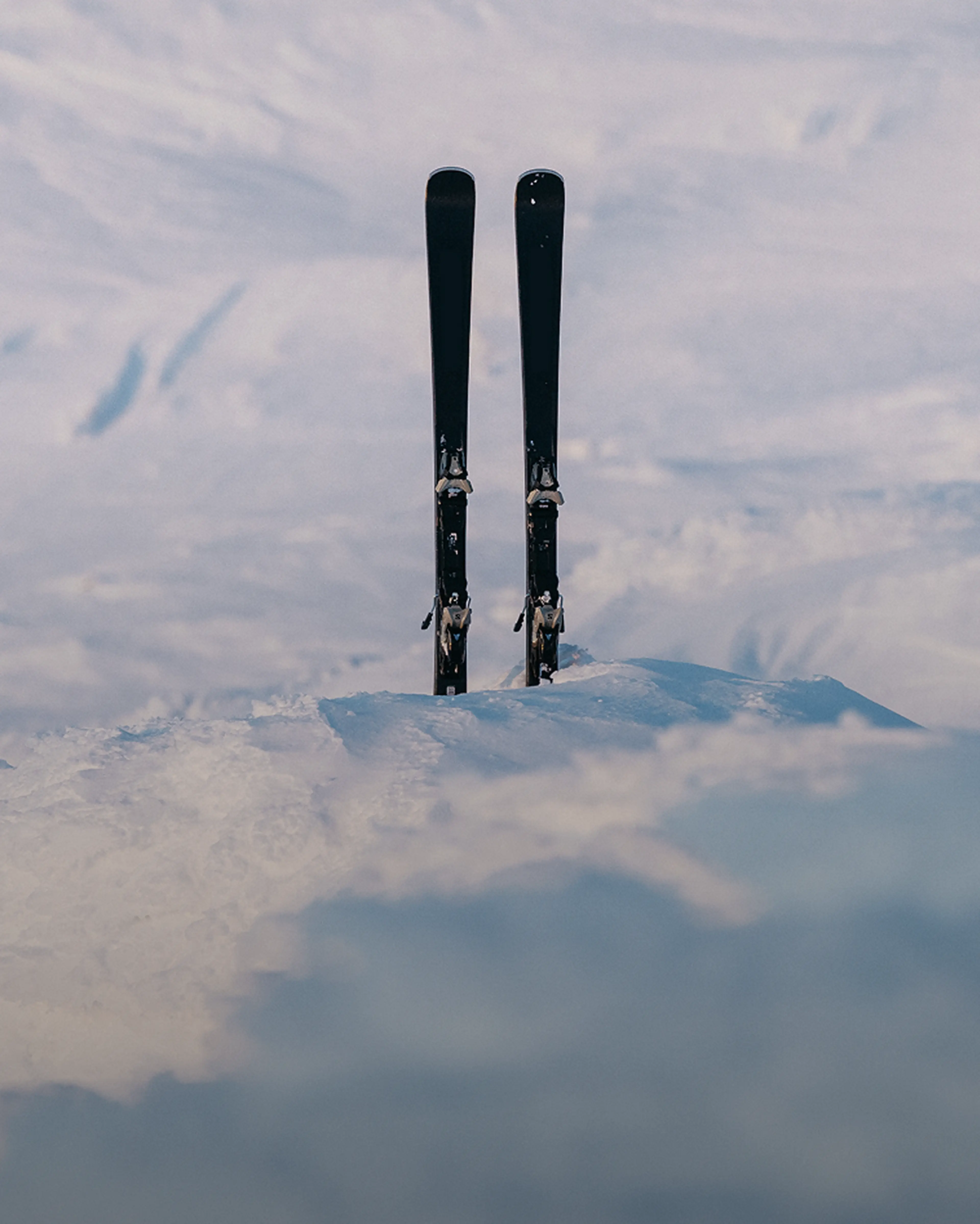 Two skis standing upright in the snow with a snowy mountain backdrop.