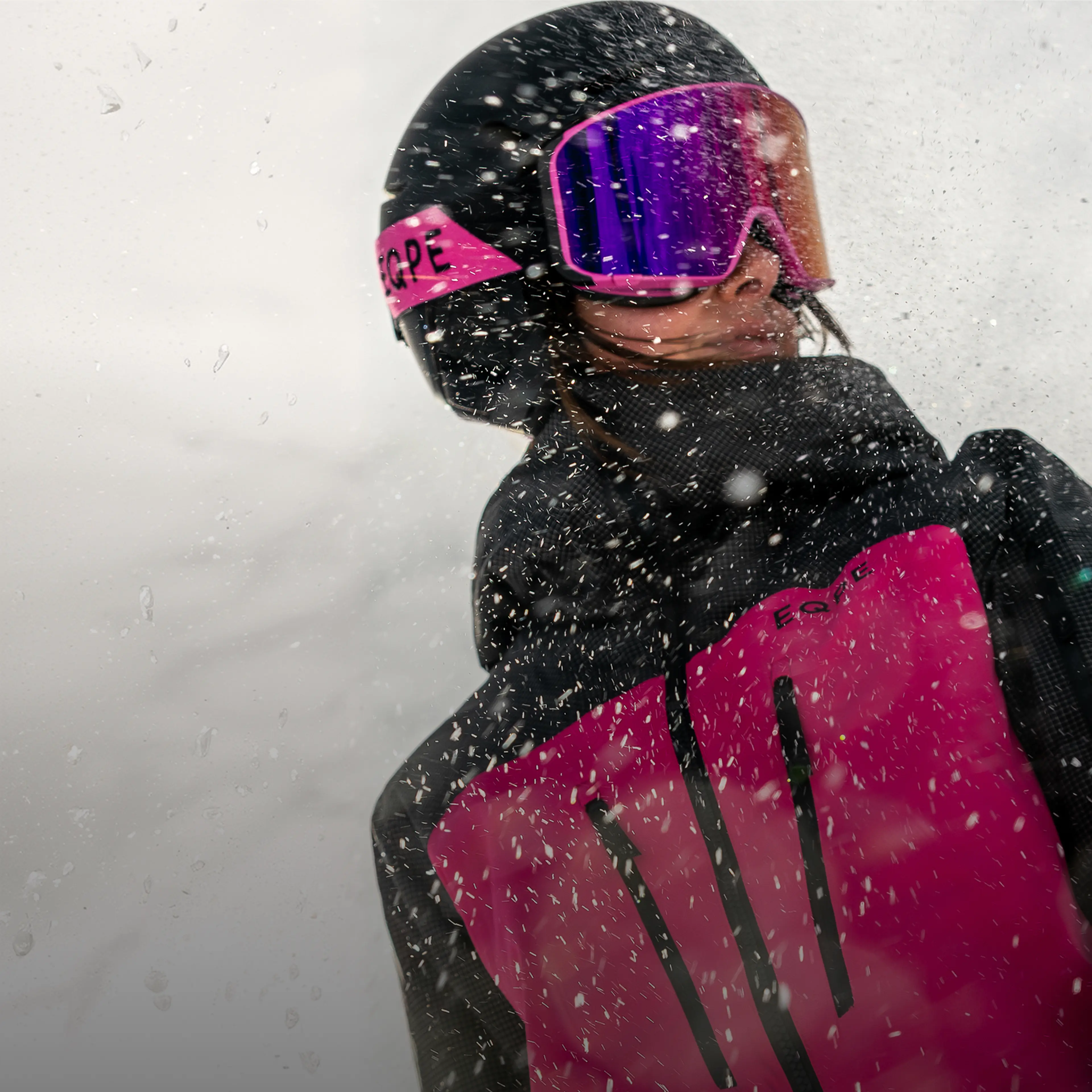 Person in pink and black snow gear, wearing goggles and helmet, facing a snowy storm.