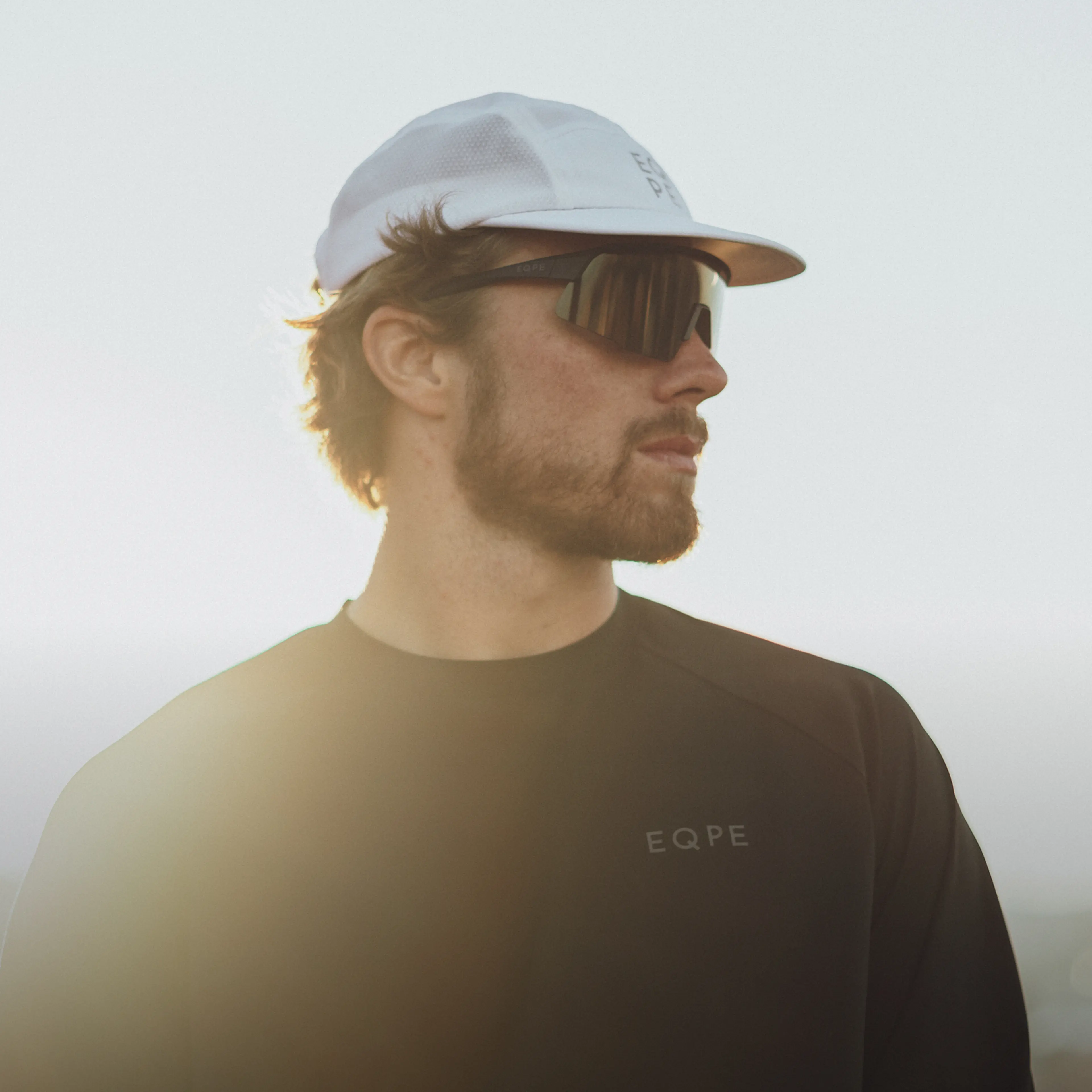 Man wearing black sunglasses, looking to the side, with sunlight creating a soft glow around him.