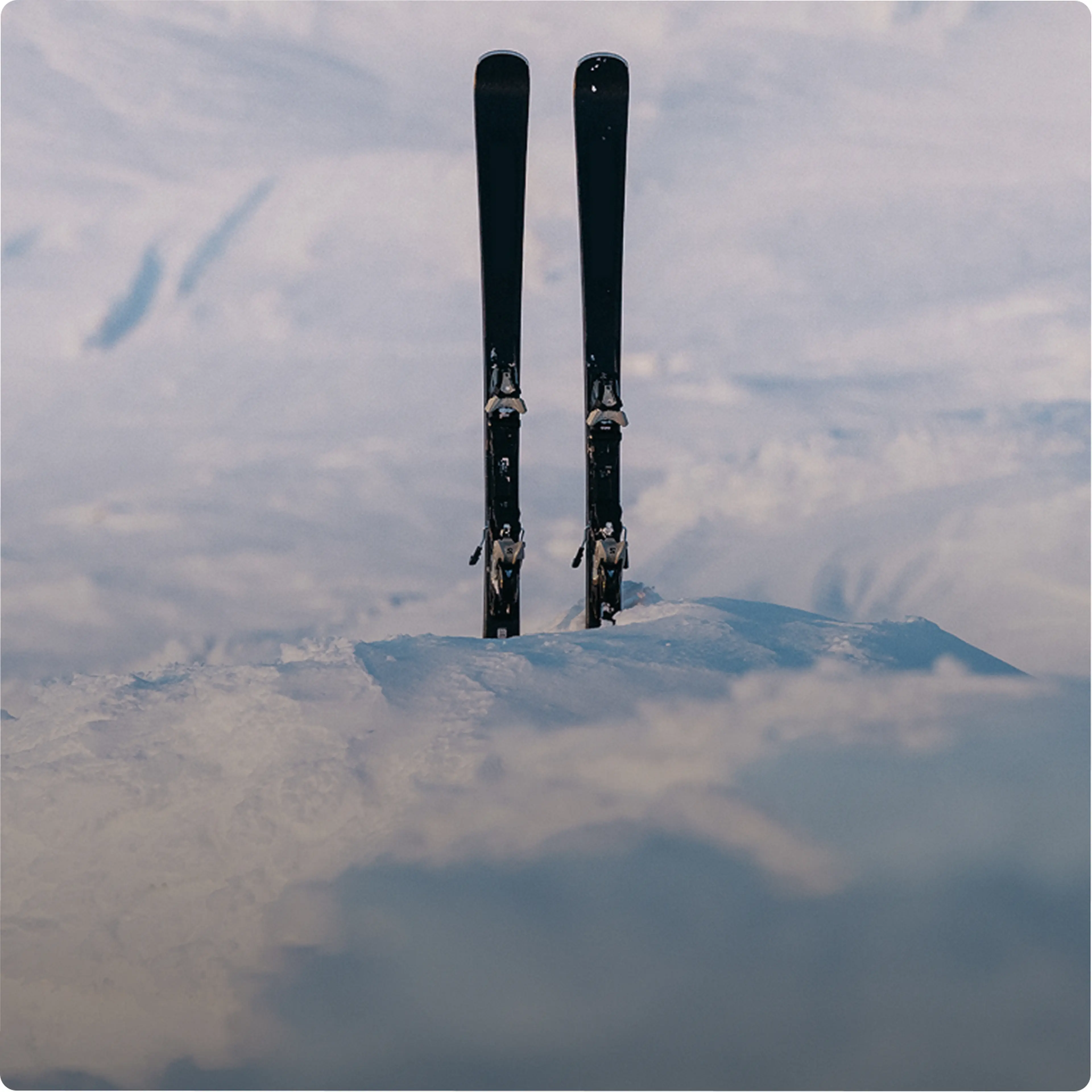 Two black skis standing upright in the snow against a background of a snowy landscape.