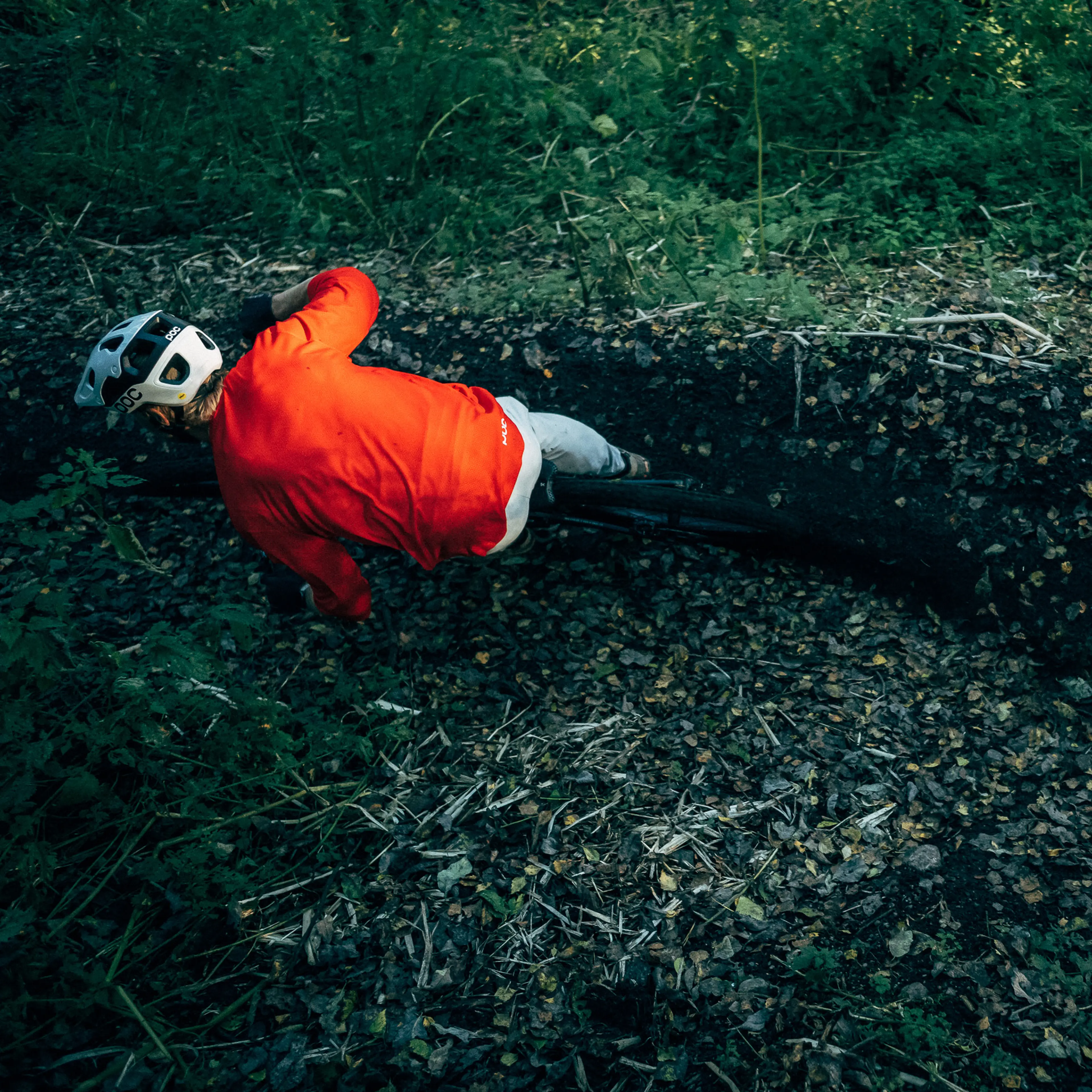 Mountain biker wearing POC rides through a leafy forest path, leaning into a curve.