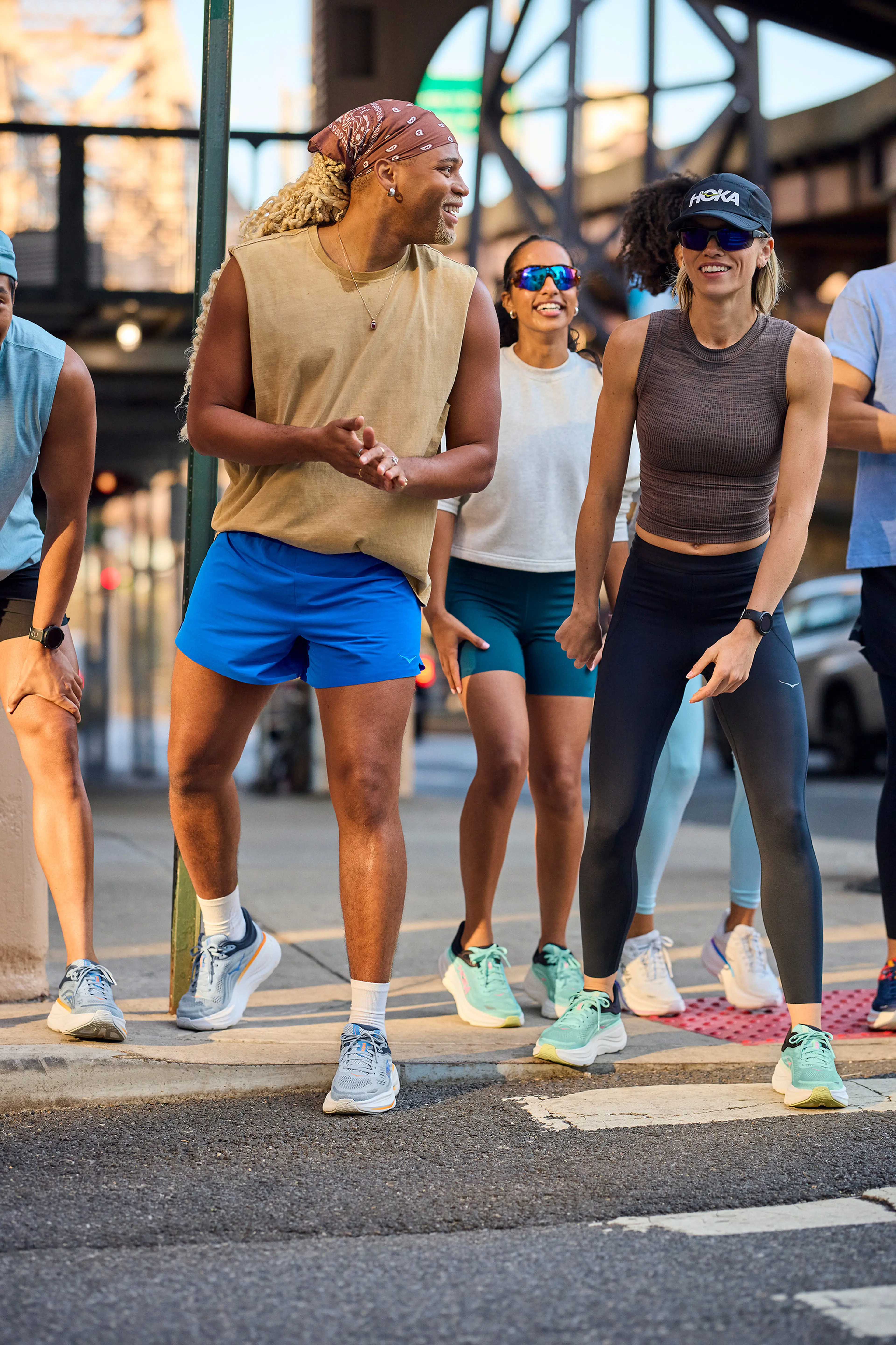 A diverse group of people smiling and warming up for a run on a city street, wearing athletic gear and sneakers.