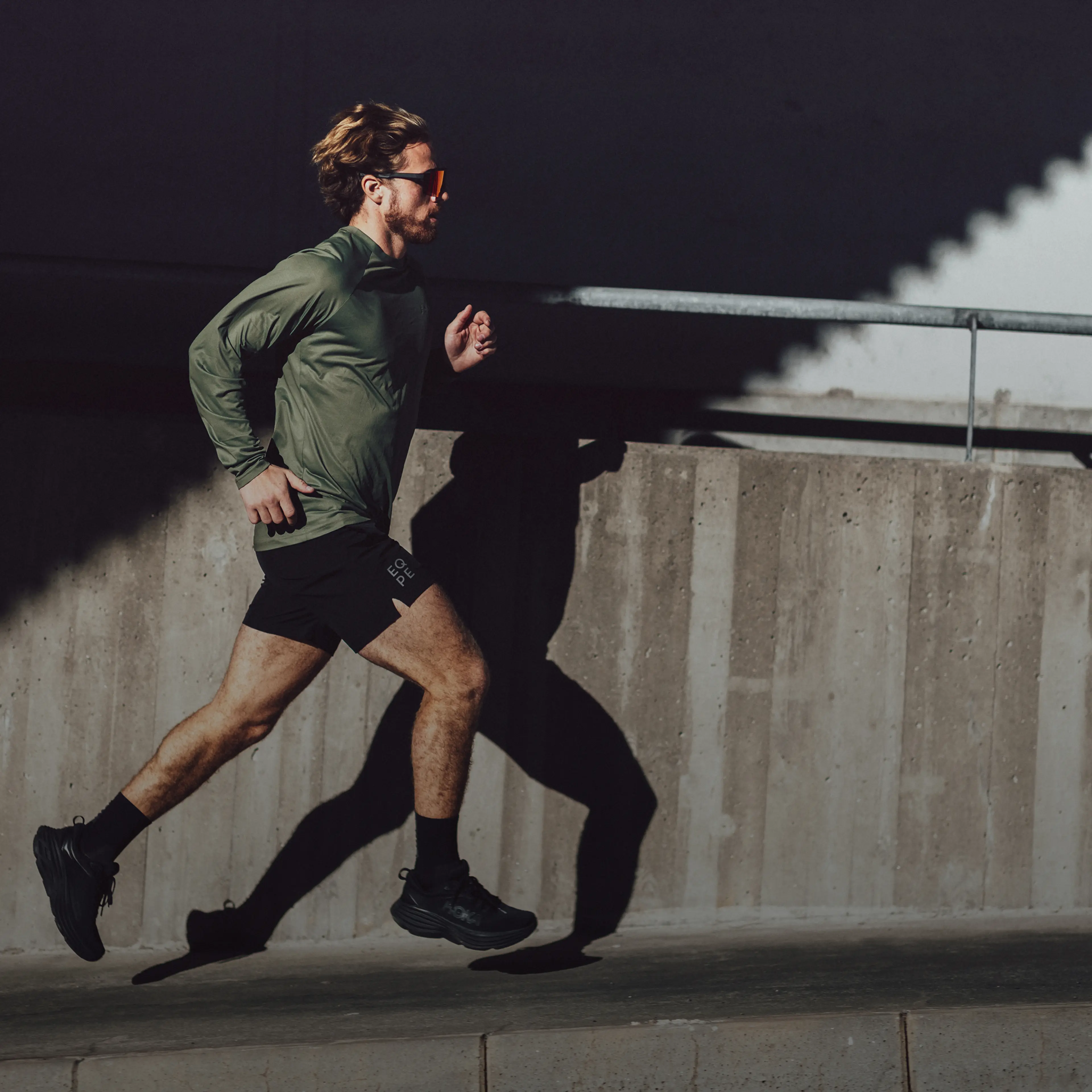 A man runs outdoors, casting a shadow on a concrete wall in bright sunlight.